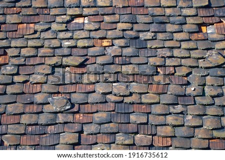 Picture of an old, wheathered roof, awaiting renovation, with coloric ceramic roof tiles in bad condition; color photo.    
   