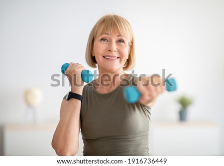 Home training concept. Strong senior woman doing exercises with dumbbells indoors. Cheerful mature lady working out her arm muscles, keeping fit, leading healthy lifestyle during covid-19 isolation Royalty-Free Stock Photo #1916736449