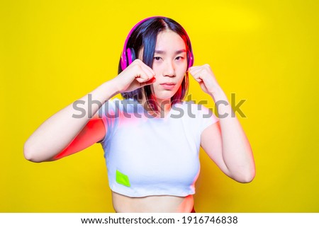 Asian sportive young woman training boxing on yellow background practicing with attitude and confidence listening music