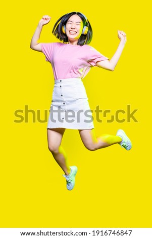 Young asiatic woman jumping on yellow background listening music - Excited youthful energetic asian woman enjoying music isolated - excited, enjoying, having fun concept