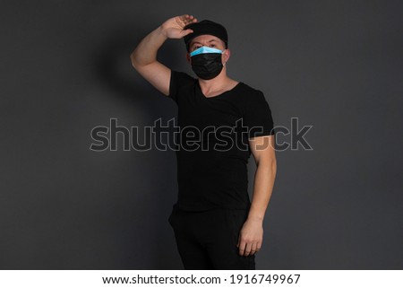 double mask. Portrait of a young man in black clothes and a cap, in two masks, dressed one on top of the other, blue and black.
