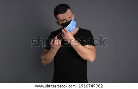 double mask. Portrait of a young man wearing black clothes and a disposable protective mask putting on a second mask in a row