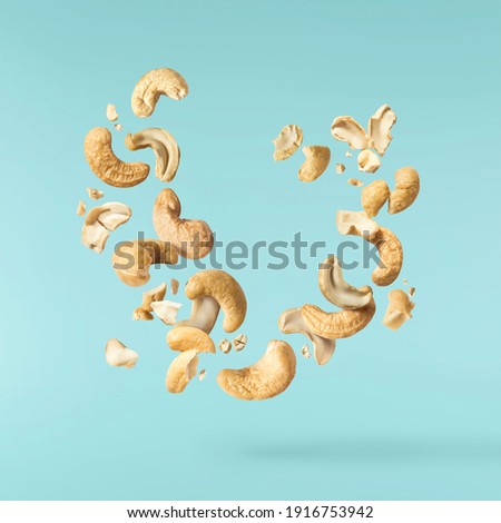 Fresh tasty Cashew nuts falling in the air isolated on turquoise background. Food levitation concept. High resolution image. Royalty-Free Stock Photo #1916753942