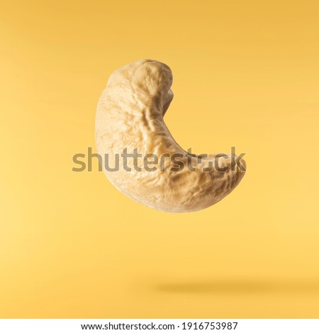 Fresh tasty Cashew nuts falling in the air isolated on yellow illuminating background. Food levitation concept. High resolution image.
