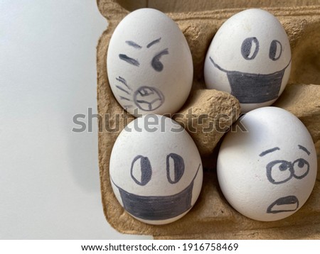 
Four white chicken eggs with funny faces lie in cartoon box on a white background. painted eggs with emotions: with eyes and in a mask, sad and surprise. preparation for Easter. creativity