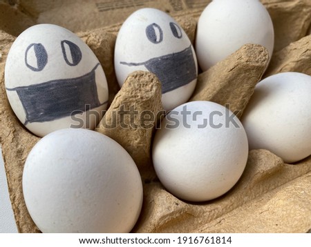 six white chicken eggs lie in cartoon box background. painted eggs with emotions: with eyes and in mask, afraid and waiting. preparation for Easter. Protection from corona virus showing in creativity