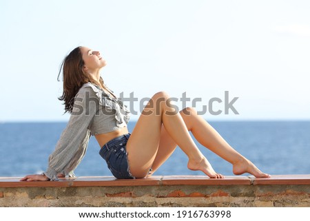 Profile of a beauty woman with perfect waxed legs sitting breathing fresh air on the beach Royalty-Free Stock Photo #1916763998