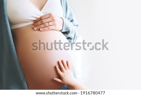 Concept of Family, Pregnancy, Motherhood, New Life. Close-up beautiful pregnant woman belly with her hand and little child hand. Expectant mother and kids waiting for baby birth.