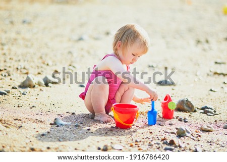 Adorable toddler girl playing with sand on the beach. Child spending vacation on the Atlantic coast in Normandy, France. Outdoor activities for kids