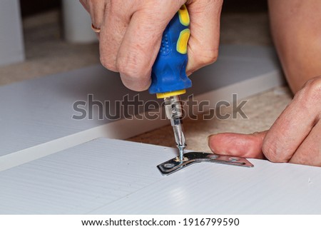 The screwdriver twists the screw into a brown wooden board in the corner, horizontal photo