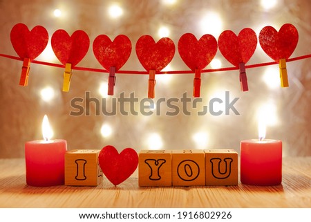 peach background with yellow garlands, at the top of the frame is a red ribbon with red hearts, at the bottom of the frame at the edges of red candles, in the center the inscription i love you