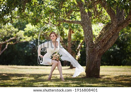 Romantic Boudoir Bride's morning outdoor in a garden. Pretty young Bride near a swing, veil flying in the wind. Beautiful redhead woman in blooming garden in her wedding day. Portrait in sunset light Royalty-Free Stock Photo #1916808401