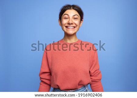 Horizontal shot of carefree positive young female with facial piercing smiling broadly at camera, raising eyebrows, expressing excitement after job promotion, winning in lottery or birthday present