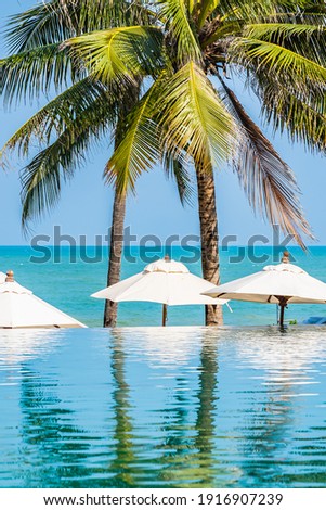 Umbrella and chair around outdoor swimming pool with coconut palm tree on blue sky white cloud