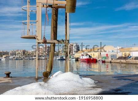 There is a pile of ice on the quay wall in the port of Torrevieja. This is used to fill fishing trawlers. In the background is the harbor basin with many boats.