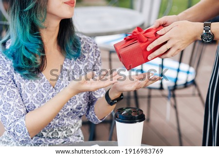 Cropped image of young woman accepting birthday present from friend when sitting at cafe table