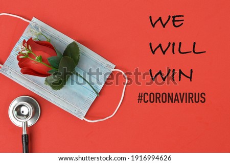 Top view of stethoscope, flower and face mask over red background written with text WE WILL WIN #CORONAVIRUS