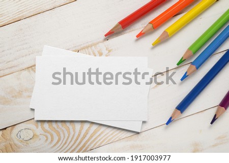 Mockup of business cards stack with colored pencils on wood plank tabletop.
