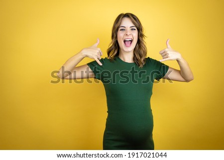 Young beautiful brunette woman pregnant expecting baby over isolated yellow background shouting with crazy expression doing rock symbol with hands up