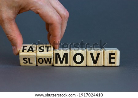 Time to fast move symbol. Businessman turns a wooden cube and changes words 'slow move' to 'fast move'. Beautiful grey table, grey background, copy space. Business and slow or fast move concept.