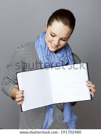 Portrait of a smiling young woman, with long brunette hair, on gray studio background, holding an open photobook or album in her hands 