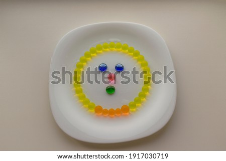 Sketchy face is laid out on a white plate of colored balls and glass stones.