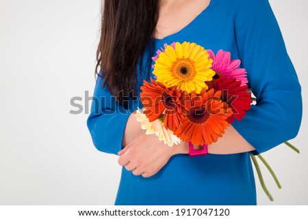Close-up of a girl with a bouquet of beautiful gerberas in her hands. Girl in a blue dress holding a bouquet of bright multicolored summer flowers
