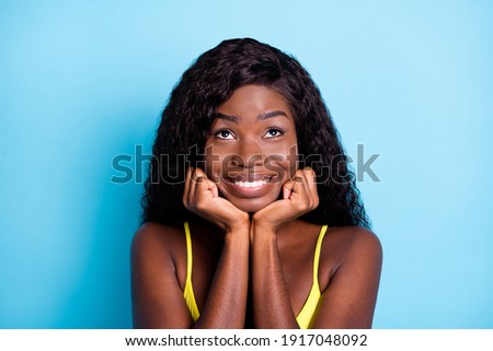 Photo of funny sweet dark skin wavy lady wear yellow tank-top arms chin looking up empty space isolated blue color background