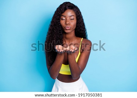 Photo pretty sweet dark skin curly girl dressed yellow singlet sending you kiss arms closed eyes isolated blue color background