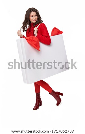 Full length portrait of young beautiful attractive brunette girl smiling and looking away while standing with white large shopping bag. White Background. Sale concept. Stock photo