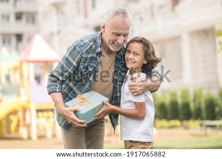 Happy family. Gray-haired man holding a gift box and hugging his son