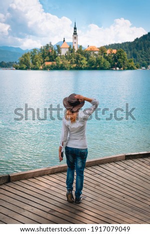 Travel Slovenia, Europe. Back view of young woman posing alone. In a white shirt with sunglasses and a cowboy hat. Bled Lake and Alps Mountain. amazing touristic attractions. Vertical photo