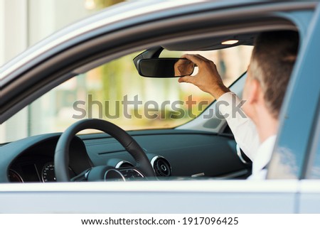 Man sitting in a car and adjusting rearview mirror, car interior Royalty-Free Stock Photo #1917096425