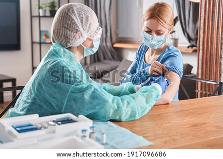 Doctor making vaccination to blonde woman patient while discussing something. Flu vaccination injection on arm, coronavirus, covid-19 vaccine disease preparing for human clinical trials vaccination Royalty-Free Stock Photo #1917096686