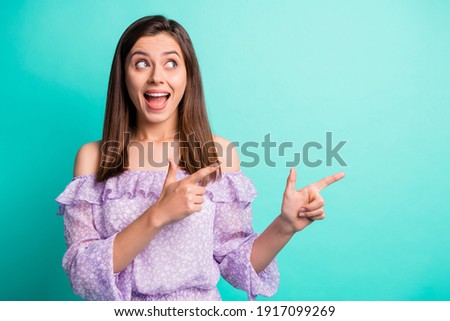 Portrait of impressed funny brunette girl pointing look empty space wear purple shirt isolated on blue color background