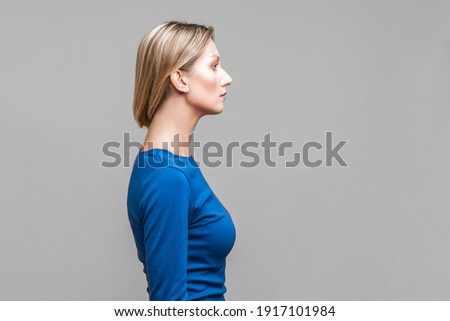 Side view of beautiful serious woman in elegant blue dress showing her neck with clean young skin, beauty skincare concept, copy space on right side. indoor studio shot isolated on gray background