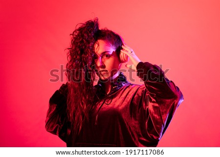 Young girl with her brown curly hair in a ponytail wearing headphones, against red background
