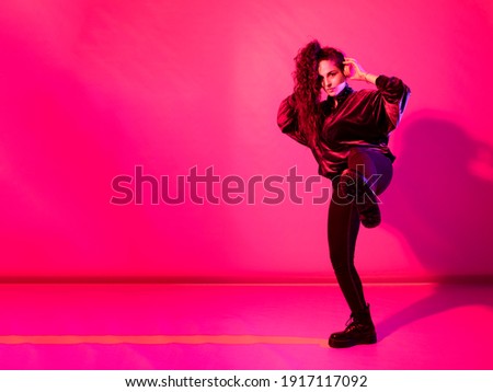Young girl with brown curly hair in a ponytail wearing headphones giving a kick, against red background