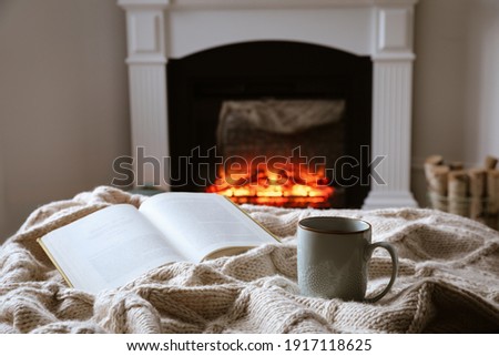 Cup of hot tea and book near fireplace at home. Cozy atmosphere