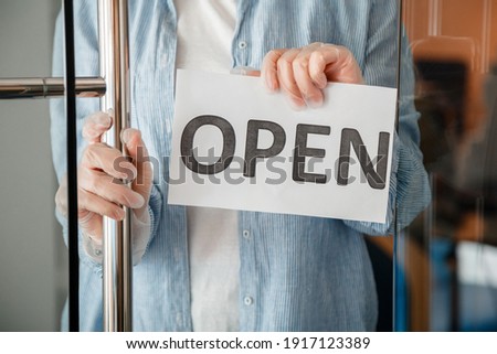 Young woman in gloves hangs on front door of cafe reopen Sign. Sign Open welcome on shop entrance door as new normal. End lockdown coronavirus covid 19 for Local business.