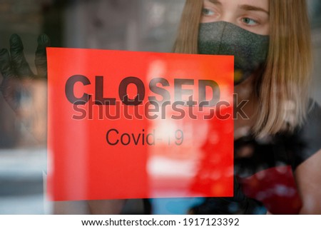 Sign Closed covid 19 lockdown on front entrance door as new normal shutdown in restaurant. Woman in protective medical mask gloves hangs closed sign on window of empty cafe. Small business crisis.