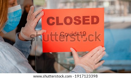 Red Sign Closed covid 19 lockdown on shop front entrance door as new normal shutdown. Woman in protective medical mask gloves hangs closed sign on window. Lockdown coronavirus covid19 Long web banner.