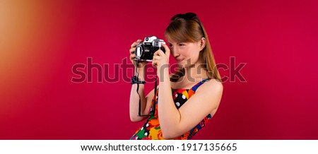 Banner, long format. A young blonde girl in summer colored clothes with sunglasses on her head takes pictures on a red background looking side with space for text or advertising. High quality photo