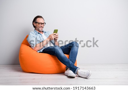 Full body photo of cheerful man happy smile seat bean bag chat type browse cellphone isolated over grey color background