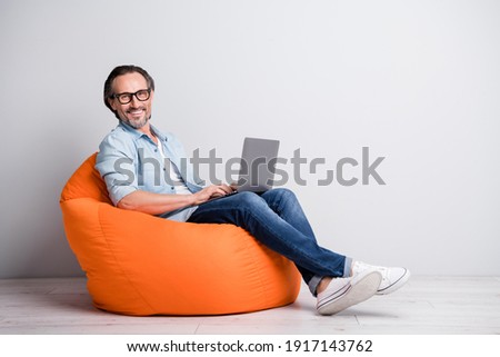 Full length photo of cheerful aged man happy smile sit chair programmer chat type laptop isolated over grey color background