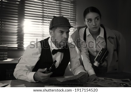 Old fashioned detective with his colleague working in office. Black and white effect