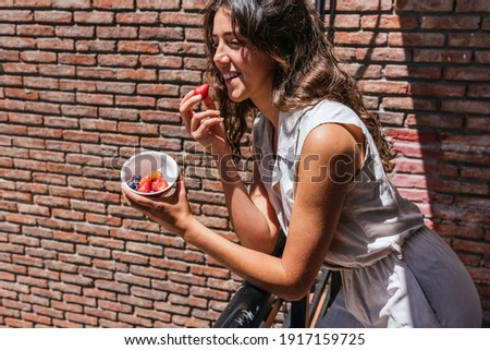 Stock photo of happy woman eating fruit in the balcony with the sun in the face.