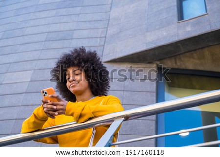 Happy millennial mixed race girl in the street of the city. Positive young african american woman web surfing, searching information, shopping in online store outdoors