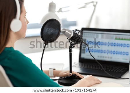 technology, mass media and people concept - close up of woman with microphone and laptop computer talking and recording podcast at studio