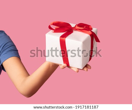 Greeting And Celebration Concept. Closeup of unrecognizable young woman holding and showing wrapped present box to camera, giving gift isolated over pastel pink studio background Royalty-Free Stock Photo #1917181187